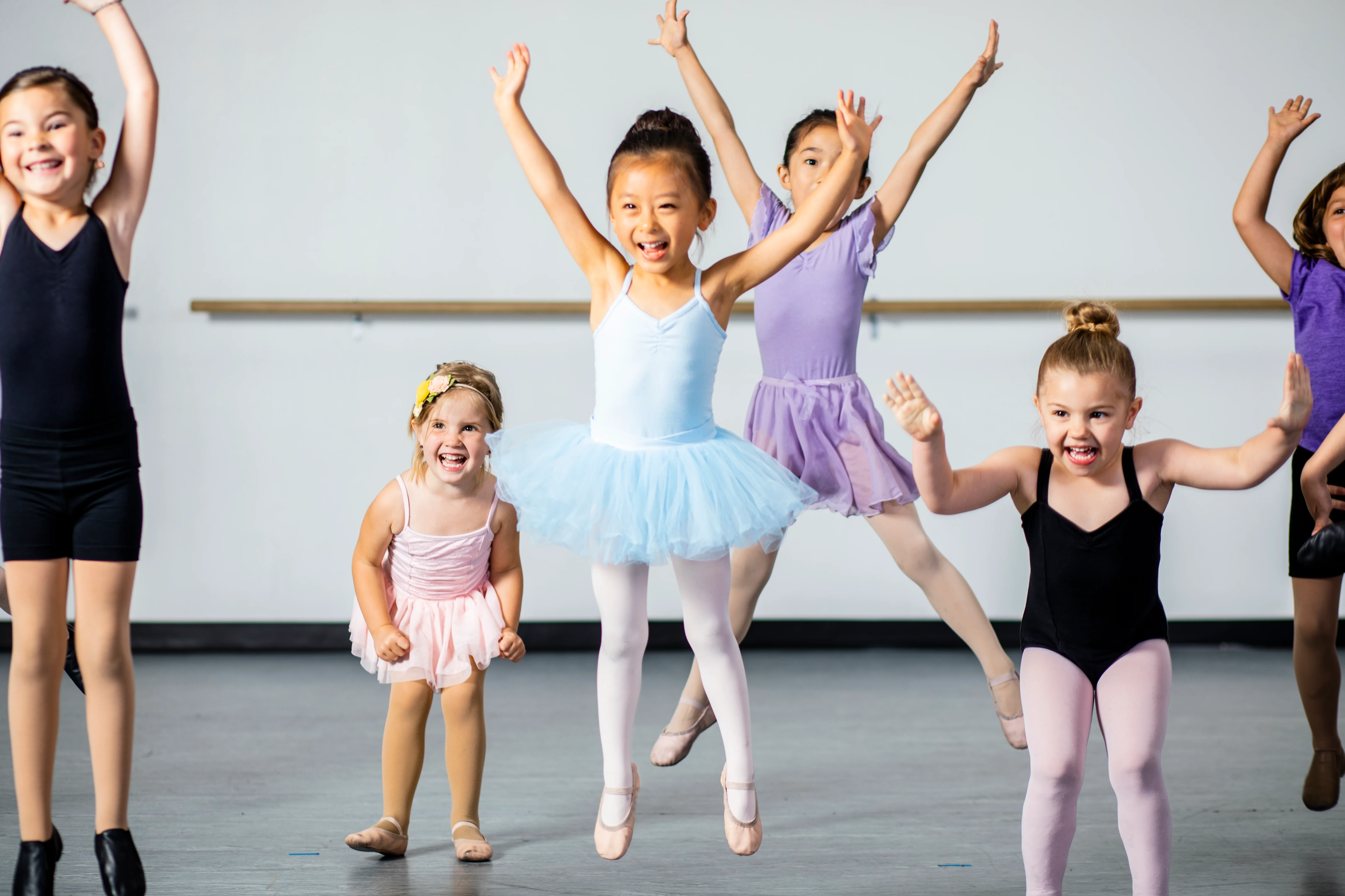Young dancers in leotards and tutus jumping with their arms up, laughing
